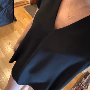 Svart kort klänning  med v-ringning - Säljer en svart kortklänning med v-ringning. Klänningen har korta ärmar och en lös passform som ger en avslappnad men stilren look. Perfekt för dig som gillar minimalistisk stil.