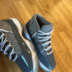 Jordan 11 Cool Grey - Säljer ett par gråa Nike Air Jordans med vita snören och sula. Skorna har en blank finish och hög modell som ger en sportig vibe. Perfekta för dig som gillar streetwear och sneakers med stil.