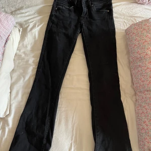 Svarta bootcut jeans - Säljer ett par svarta bootcut jeans med klassisk femficksdesign och normal passform. Jeansen har dragkedja och knapp framtill samt bälteshällor. Perfekta till många olika outfits.
