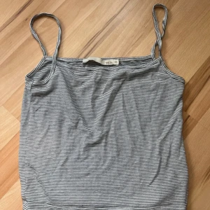 Randig linne-topp - Säljer en smalrandig linne-topp i svart och vitt med tunna axelband. Perfekt för varma dagar eller som lager under andra plagg. Enkel och stilren design som passar till mycket.