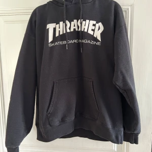 Svart Thrasher hoodie - Svart hoodie från Thrasher med vit logga. Klassisk känguruficka framtill och justerbar huva med snören. Storlek M 