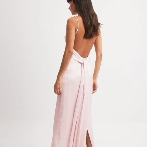 Ljusrosa långklänning i satin med öppen rygg - Säljer en elegant ljusrosa långklänning i satin med smala axelband och öppen rygg från NAKD. Klänningen har en slits bak och en snygg detalj med knyt i midjan. Perfekt för balen ❤️❤️❤️ Aldrig använd 💕
