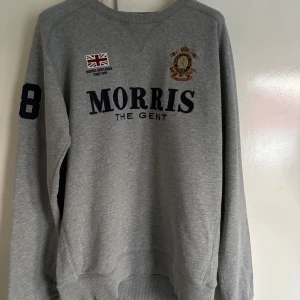 Grå sweatshirt från Morris - Grå sweatshirt från Morris med tryck och broderad logga på bröstet samt siffran 8 på ärmen. Klassisk rund halsringning och ribbade muddar. Perfekt för en avslappnad stil.