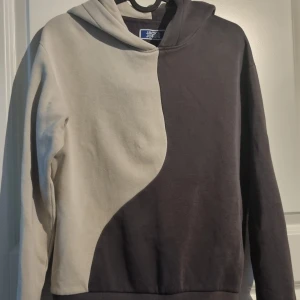 Tvåfärgad hoodie från Jack & Jones - Säljer en hoodie från Jack & Jones i tvåfärgad design, ena sidan är beige och andra sidan grå. Tröjan har huva och är långärmad, perfekt för en avslappnad stil.