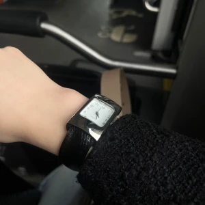 Svart och silver damklocka med skinnarmband - Stilren damklocka med svart skinnarmband och rektangulärt silverfärgat ur. Tydlig vit urtavla med svarta siffror och visare. Klockan har en modern design med breda band och passar perfekt som accessoar.