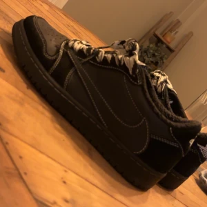 Travis Scott Black Phantom Jordan 1 - Snygga svarta jordan Travis Scott med vit snörning och perforerad tå. Skorna har en broderad detalj på hälen och en klassisk Air Jordan-logga. Perfekta för en stilren streetwear  look. Kommer även med svarta sko snören bara att skriva för mer frågor