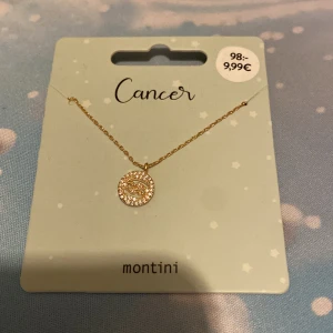 Guldigt halsband med Cancer-stjärntecken från Montini - Snyggt halsband i guld från Montini med ett runt hänge som har Cancer-stjärntecknet. Perfekt accessoar för dig som vill visa ditt stjärntecken. Kedjan är tunn och elegant.
