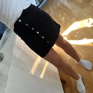 Svart kjol med knappar från JDY Denim - Svart kortkjol från JDY Denim med silverfärgade knappar framtill. Kjolen har en rak passform och är enkel att matcha med olika toppar. Perfekt för dig som gillar en stilren och klassisk look.