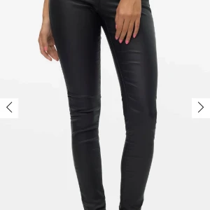 Svarta byxor i skinnimitation från Vero Moda - Snygga svarta byxor i skinnimitation från Vero Moda med medelhög midja och tight passform. 