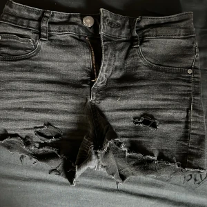 Svarta jeansshorts från C Denim - Svarta jeansshorts från C Denim, modell Jegging Jane. De har fransiga benslut, slitna detaljer och klassisk femficksdesign. Mid rise-modell med knapp och dragkedja framtill. Perfekta för en avslappnad stil.