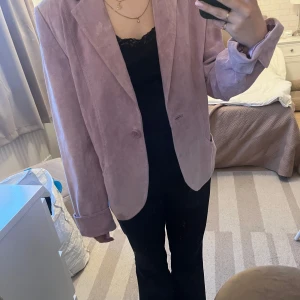 Ljuslila mockakavaj  - Säljer en ljuslila kavaj i äkta mocka.Kavajen har klassisk krage, en knapp framtill och är helfodrad med glansigt lila polyestersatin. Perfekt för dig som vill sticka ut med en färgglad och stilren look. Det finn mindre fläckar, har inte försökt ta bort så vet ej om de går 