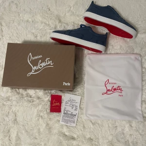 Blå sneakers från Christian Louboutin - Säljer ett par blå sneakers från Christian Louboutin med klassisk röd sula. Skorna har snörning och rund tå, ovandel i mocka och vit platt sula. Inkluderar originalkartong och dustbag.