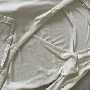 Vit blus från Nelly - Säljer en vit blus från Nelly i storlek XS. Klänningen har en snygg omlottdesign och är tillverkad i ett mjukt material som känns skönt mot huden. Perfekt för dig som gillar stilrena och enkla plagg.