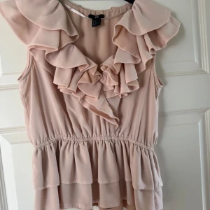 Ljusrosa volangblus från H&M🩷 - Supersöt ljusrosa blus med volanger runt halsringningen och axlarna. Ärmlös modell med markerad midja och lätt utsvängd nederdel. Slutsåld överallt och säljs inte längre. Storleken är mindre i storleken skulle säga den passar mellan L, M och S.❤️