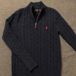 Mörkblå stickad tröja med dragkedja från Polo Ralph Lauren - Säljer en mörkblå kabelstickad tröja från Polo Ralph Lauren med halv dragkedja. Skick 10/10 sällan använd. Tröjan visar inga tecken på skador