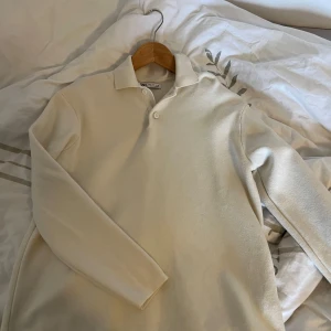 Vit långärmad pikétröja  - Säljer en stilren vit långärmad pikétröja från Oscar Jacobson. Tröjan har klassisk krage och knäppning framtill, perfekt för en clean och avslappnad look. Passar lika bra till jeans som till chinos.