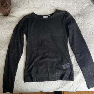 Svart glittrig meshtröja från Kappahl - Säljer en svart långärmad meshtröja från Kappahl med glittrigt mönster. Tröjan är genomskinlig och har en tight passform, perfekt att styla över ett linne eller bh. Superfin till fest eller när du vill sticka ut lite extra! Storlek XS