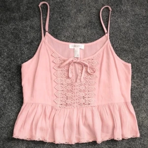 Rosa linnetopp med spets och volang från Forever 21 - Söt ljusrosa linnetopp med smala axelband, spetsdetaljer och knyt framtill. Volang nertill ger en romantisk känsla. Perfekt för varma dagar.
