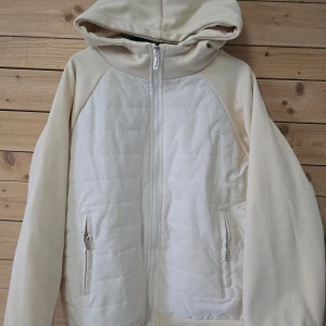 Beige quiltad hoodiejacka med dragkedja - Oanvänd Snygg beige hoodiejacka med quiltad framsida och dragkedja. Jackan har huva och två fickor med dragkedja. Perfekt för lager-på-lager och chill vardagsstil.  Skulle säga storlek är ca 164