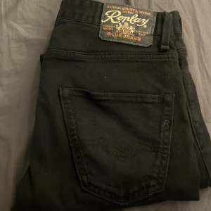 Svarta jeansbyxor från Replay - Säljer ett par svarta jeans från Replay med klassisk femficksdesign och Replay-logga på bakfickan. Byxorna har normal passform och är tillverkade i ett mjukt jeanstyg. Perfekta för dig som gillar stilrena och tidlösa jeans.