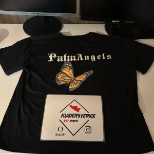Svart t-shirt från Palm Angels med tryck - Svart t-shirt från Palm Angels med vit text på framsidan och stort logotryck samt fjäril på ryggen. T-shirten har rund hals och normal passform. Perfekt för dig som gillar streetwear och snygga detaljer.