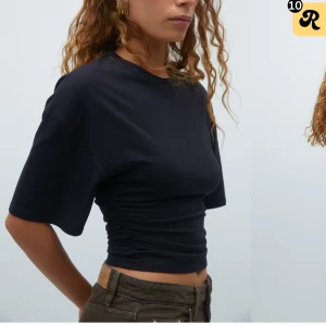 Svart croppad t-shirt med rynkade detaljer - Snygg svart t-shirt med korta ärmar och croppad passform. T-shirten har rynkade detaljer i midjan som ger en cool och trendig look. Perfekt till jeans eller kjol för en avslappnad stil. Fick precis hem den. Så helt oanvänd 