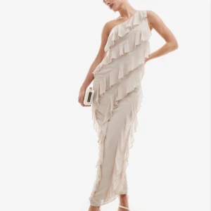 Champagnefärgad balklänning  - E champagnefärgad långklänning med volangdetaljer och oneshoulder-design. Bär den med klackar och en liten clutch för en stilren look. Klänningen är från ASOS, TFNC petite🫶perfekt för bal