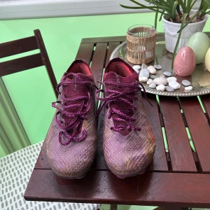 Lila och röda fotbollsskor med snörning - Säljer ett par lila fotbollsskor med röda och gula detaljer. Skorna har snörning och är designade för att ge bra grepp på planen. Perfekta för dig som vill sticka ut med färg på matchen. Pris kan diskuteras skriv om ni vill ha mer bilder på skorna