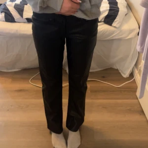 Svarta raka byxor i skinnimitation - Säljer ett par svarta byxor i skinnimitation med rak passform. Byxorna har normal midja och klassisk design utan synliga detaljer. Perfekta för dig som vill ha en stilren look. Modellen ”ICON”🥰