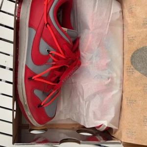 Nike Dunk i rött och grått - Snygga Nike Dunk sneakers i en cool kombination av rött och grått. Skorna har en klassisk design med snörning och en bekväm passform. Perfekta för att ge din outfit en sportig touch.