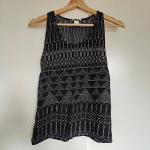 Svart och vit mönstrad linnetopp - Snygg svart och vit mönstrad linnetopp med geometriska mönster. Perfekt för varma dagar med sin ärmlösa design och bekväma passform. Ett stilrent val för en avslappnad look.