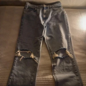 Ljusa jeans med slitningar - Säljer ett par ljusa jeans med coola slitningar på knäna. De har en klassisk femficksdesign och en knappgylf. Perfekta för en avslappnad stil. Högmidjande jeans