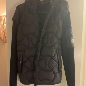 Svart jacka från Moncler cardigan - Snygg svart jacka från Moncler med quiltad design och dragkedja. Jackan har en huva och långa ärmar. Perfekt för kyligare dagar med sin stilrena look. Använd 2-3 gånger endast så cond 9/10, självklart äkta, nu pris 11 999