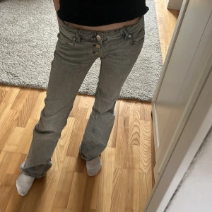 Grå jeans med knappar - Snygga grå jeans med hög midja och bootcut-stil. De har en unik knappdetalj framtill och är perfekta för en trendig look. Passar bra till både vardag och speciella tillfällen.Grå jeans från Gina tricot i strl 146 tall, de är insydda i låren.