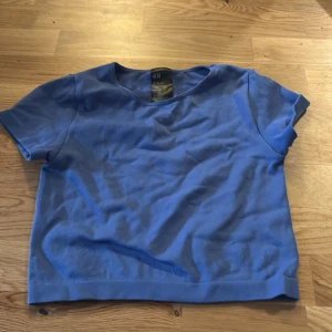 Blå kortärmad topp från H&M - Säljer en enkel och stilren blå kortärmad topp från H&M. Perfekt för en avslappnad look. Toppen har en rund halsringning och är gjord i ett mjukt material.