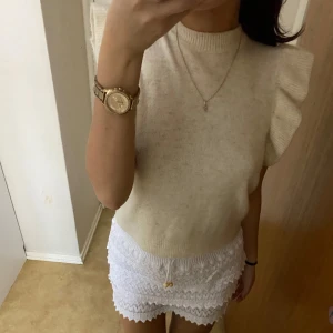 Beige stickad topp med volangärmar - Nyskick! Från vila 💕köpte för 499kr Säljer en stilren beige stickad topp med volangdetaljer på ärmarna. Toppen har en rund halsringning och är perfekt för en chic look. Passar bra till både kjol och byxor.