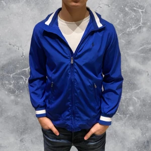 Ralph Lauren Windbreaker blå - •Ralph Lauren windbreaker jacka blå. Skick: 8-9/10, Inga skador! Storlek: 14/16 yrs ungdom= strl XS~ 160-170 cm. Modell: 173 cm, 65 kg. Sitter litet på modellen på bild! Authentic: ✅. Hör av dig vid frågor eller funderingar, mvh Hessler’s;) 