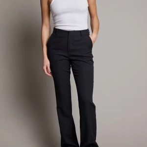 Svarta kostymbyxor - Snygga svarta kostymbyxor med hög midja och bootcut-stil. Perfekta för en stilren look. Byxorna har en klassisk design med dragkedja och knapp framtill.