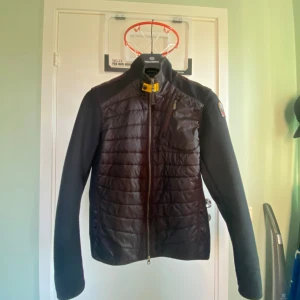 Svart jacka från Parajumpers - Säljer en svart jacka från Parajumpers med quiltad design och dragkedja. Jackan har långa ärmar och en praktisk bröstficka med dragkedja. Perfekt för kyligare dagar.