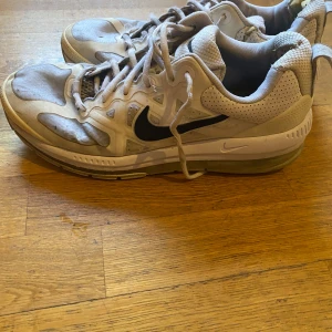 Nike Air Max Genome (GS) Triple White - Säljer ett par vita Nike Air Max sneakers med svart swoosh. Skorna har snörning och en synlig Air Max-dämpning i sulan för extra komfort. Perfekta för både träning och vardag.