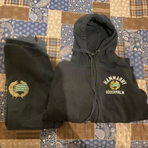 Svart tracksuit från Hammarby - Säljer en svart tracksuit från Hammarby. Hoodien har dragkedja och huva samt har Hammarby-logga på bröstet och texten 'Södermalm”. Byxorna har hammarby-logga och är svarta. Passar längd 146-152