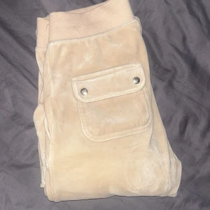 Beige mjukisbyxor med fickdetaljer - Snygga beige mjukisbyxor med elastisk midja och snörning. Byxorna har praktiska fickor med knappar både fram och bak, vilket ger en cool look. Perfekta för en avslappnad stil.