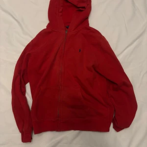 Röd hoodie från Polo Ralph Lauren - Säljer en snygg röd hoodie från Polo Ralph Lauren med dragkedja och broderad logga på bröstet. Perfekt för en avslappnad stil. Den har en klassisk passform och är tillverkad i mjukt material för extra komfort. Har inga defekter.