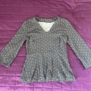 Mönstrad topp med trekvartsärm - Säljer en snygg mönstrad topp med trekvartsärm och v-ringning. Toppen har ett svart och vitt geometriskt mönster och en lätt utsvängd nederdel. Perfekt för en stilren look!🙌🤩