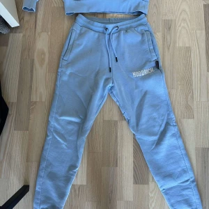 Ljusblå hoodie och byxor från Hoodrich - Säljer ett set med ljusblå hoodie och matchande byxor från Hoodrich. Hoodien har en stor ficka framtill och justerbar huva med dragsko. Byxorna har resår i midjan och dragsko för perfekt passform. Båda plaggen har Hoodrich-loggan tryckt i vitt.