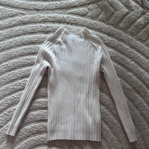 Vit ribbad tröja - Säljer en vit ribbad tröja från Extra Me. Tröjan har långa ärmar och en hög krage som ger en elegant look. Lätt att matcha med olika outfits.  Det finns ett litet hål på tröjan men syns knappt. Hör av dig vid intresse! 🤍
