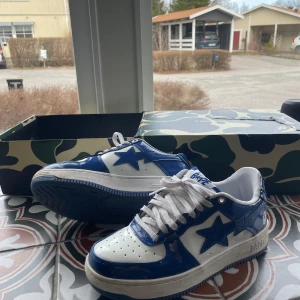 Blå och vita sneakers från BAPE - Snygga sneakers från BAPE i en fräsch blå och vit färgkombination. Skorna har en klassisk design med snörning och en stjärndetalj på sidan. Perfekta för att ge din outfit en cool touch.