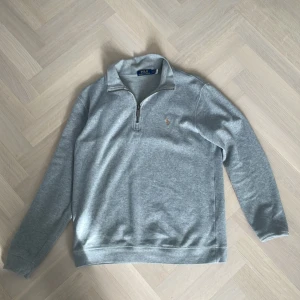 Grå tröja från Polo Ralph Lauren - Säljer en stilren grå tröja från Polo Ralph Lauren med dragkedja och broderad logga på bröstet. Tröjan har långa ärmar och är perfekt för en avslappnad look. Passar bra till både jeans och chinos. Köptes på Vinted för något år sedan, säljes pga att jag vuxit ur den. 