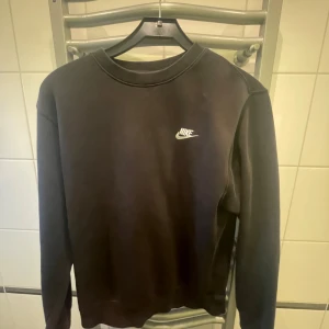Svart sweatshirt från Nike - Säljer en stilren svart sweatshirt från Nike med deras klassiska logga på bröstet. Tröjan har en rund halsringning och långa ärmar, perfekt för en avslappnad look. Passar bra till både jeans och träningsbyxor.