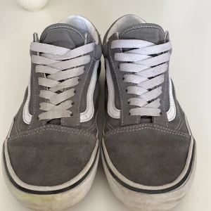 Grå sneakers från Vans - Säljer ett par klassiska grå sneakers från Vans med vit sula och snörning. Skorna har den ikoniska sidostripen i vitt och är perfekta för en avslappnad stil. De är i storlek herr 38 och passar perfekt för vardagsbruk. Priset är inte fast i sten